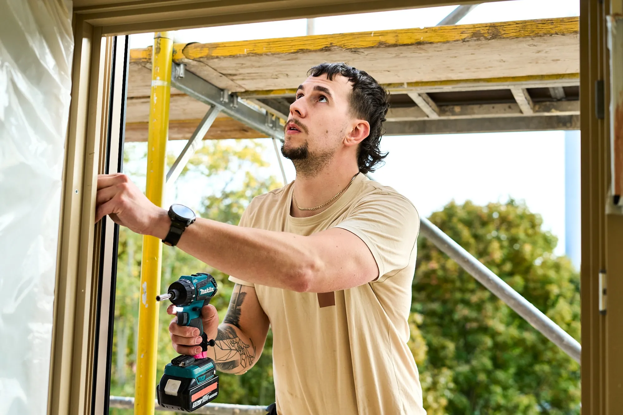 Monteur im certo-T-Shirt beim Einbau eines Fensters, draußen ein Baugerüst