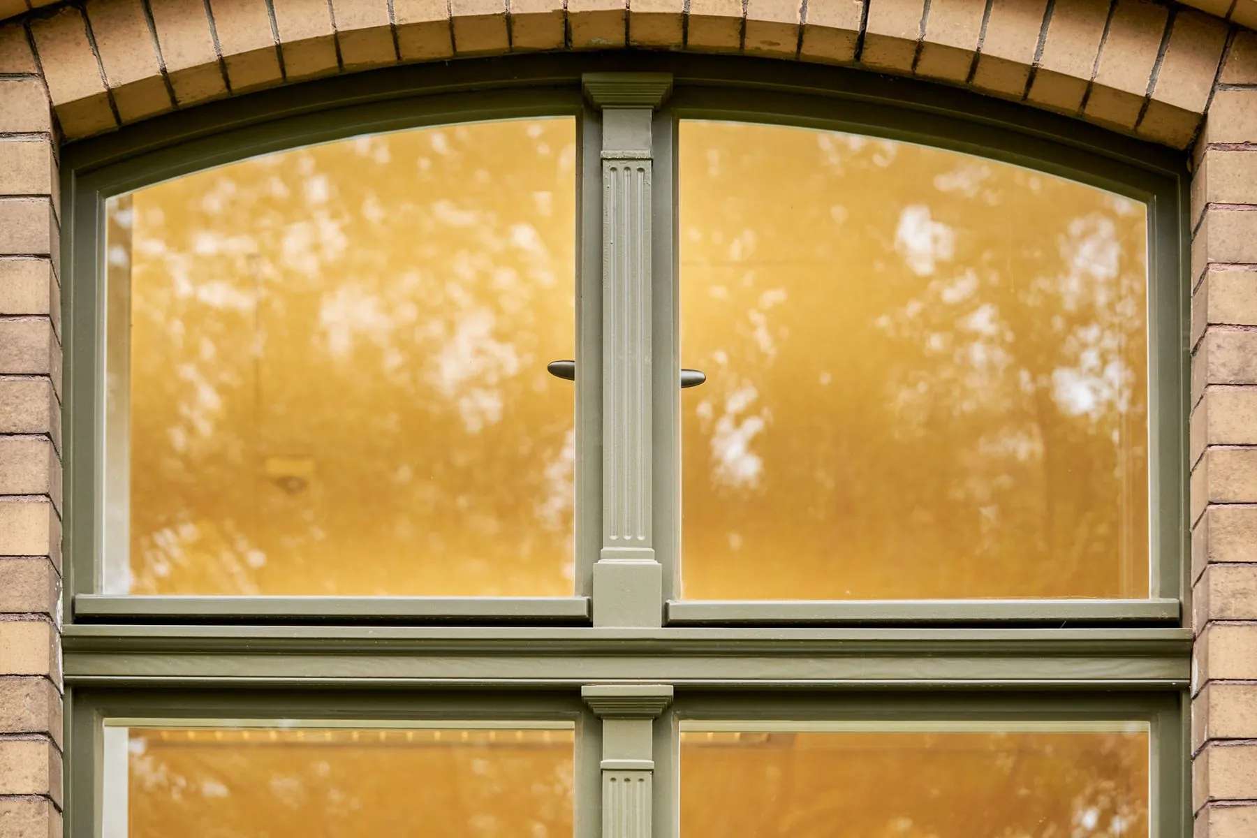 Restauriertes historisches Holzfenster mit Rundbogen in einer Klinkerfassade